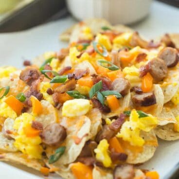 These Breakfast Nachos are topped with bacon, breakfast sausage, peppers, scrambled eggs and cheese and are perfect for your next brunch or even game day!