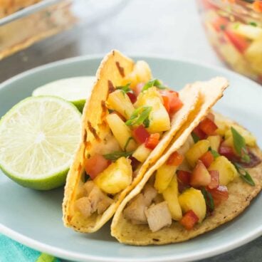 These Baked Hawaiian Chicken Tacos are perfect for game day or any gathering because you can serve a whole bunch at once! Stuffed with slow cooker coconut chicken, baked, then topped with an easy homemade pineapple salsa!