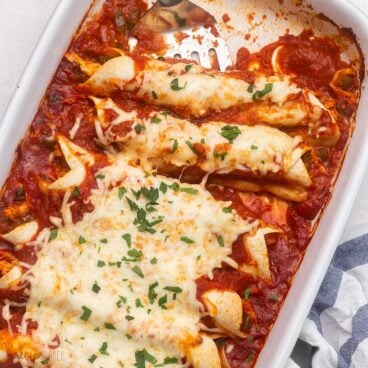 square image of red chicken enchiladas in white baking dish.