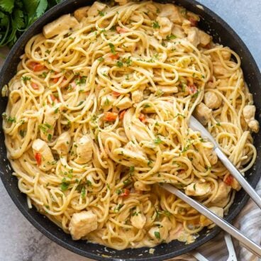 overhead image of chicken spaghetti in black skillet with tongs.