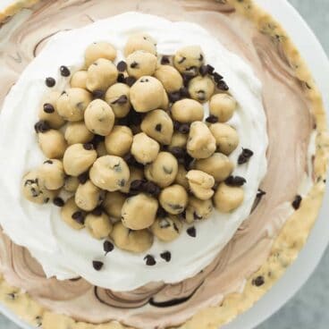 This Cookie Dough Ice Cream Cake is an easy, no bake dessert for a summer cookout or birthday party! Made on a cookie dough crust, filled with no churn ice cream and topped with chunks of cookie dough. Includes step by step recipe video | dessert recipe | cookie recipe | no bake dessert | summer | Easter | spring | birthday party