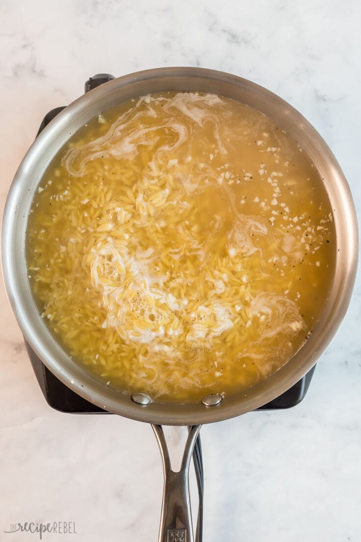 orzo cooking in broth in stainless steel skillet