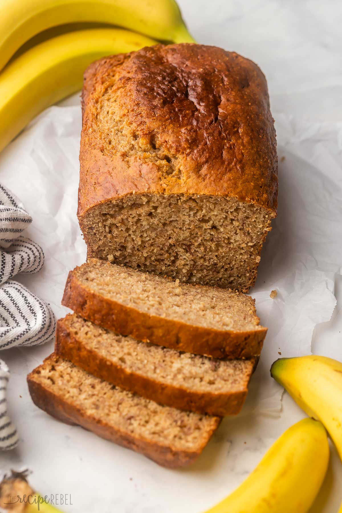 sliced healthy banana bread on parchment paper with bananas around it.