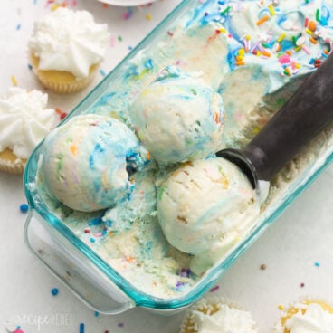 Top view close up of a glass dish filled with birthday cake ice cream with an ice cream scoop in it.