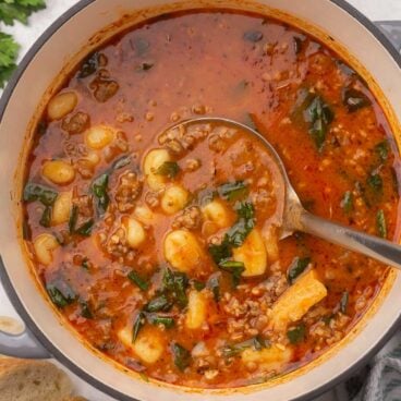 a large grey pot of sausage gnocchi soup with metal ladle in it.