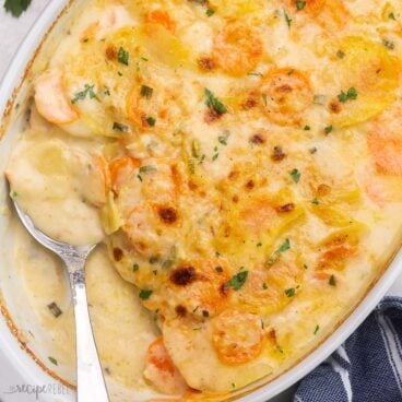 close up square shot of baked scalloped potatoes and carrots in white dish.