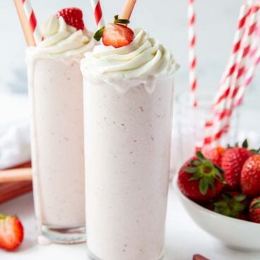 two strawberry rhubarb milkshakes in glasses with whipped cream