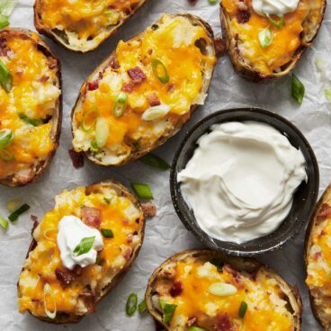 Top view of twice baked potatoes on a white plate with a small bowl of dip next to them.